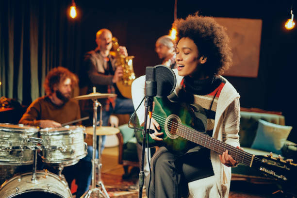 Cantante che suona la chitarra seduta; sullo sfondo batterista, sassofonista e bassista